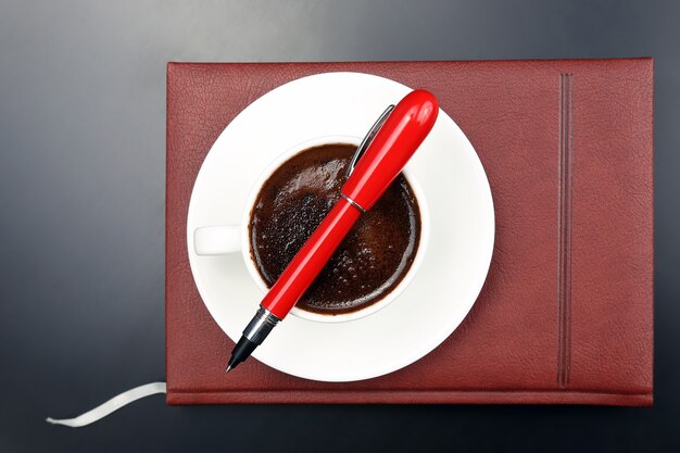 Le stylo rouge est sur la tasse avec du café noir et un cahier