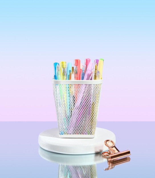 Stylos multicolores dans un gobelet à stylos sur un support rond Trombone allongé sur un miroir