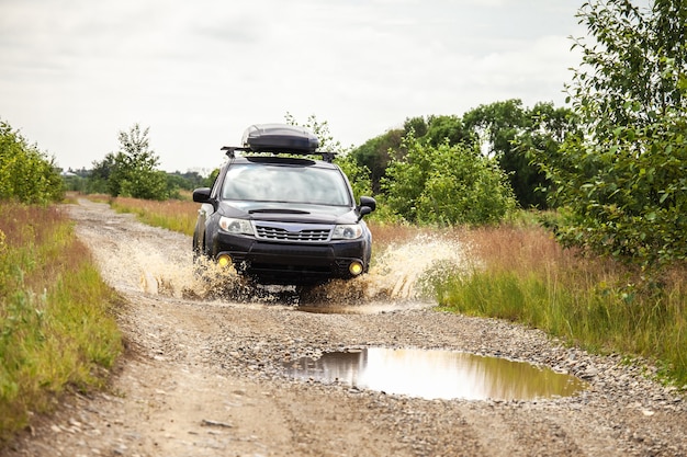 Subaru Forester noir roulant sur un chemin de terre avec des flaques d'eau. L'eau éclabousse sous les roues