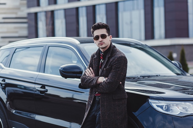 Succès, bel homme en manteau près de la voiture.