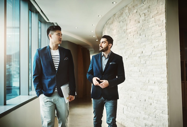 Le succès est une question de maintenant et de demain Photo de deux jeunes hommes d'affaires marchant et parlant dans un bureau moderne