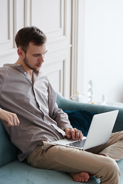 Succès heureux jeune homme d'affaires caucasien travaillant à la maison avec un ordinateur portable sur le canapé Concept d'apprentissage à distance et de travail à distance