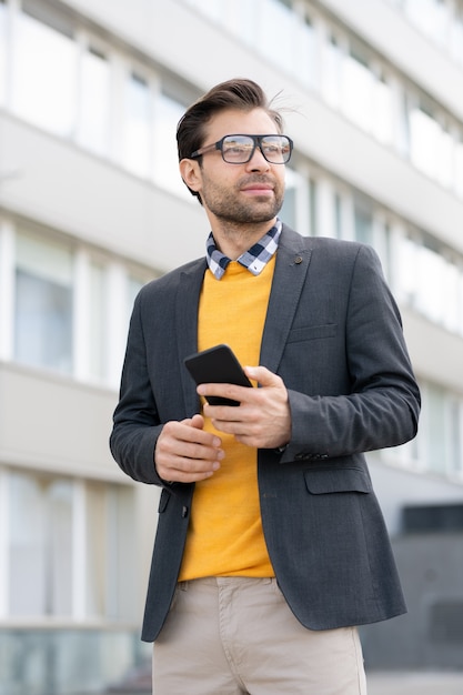 Succès jeune homme en smart casual et lunettes debout dans un environnement urbain avec une architecture moderne