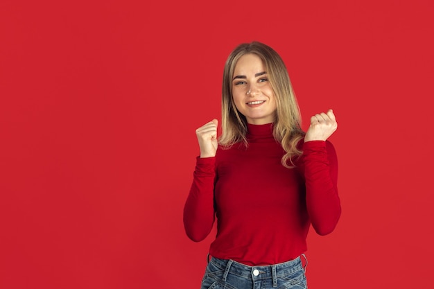 Succès. Portrait monochrome de jeune femme blonde caucasienne isolée sur mur rouge. Beau modèle féminin en chemise. Émotions humaines, expression faciale, ventes, concept publicitaire. La culture des jeunes.