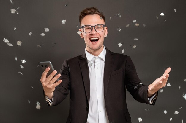 Succès professionnel Promotion spéciale Étonné homme d'affaires excité heureux avec des nouvelles de l'appel téléphonique sous la pluie de confettis isolé sur noir Fête d'entreprise amusante