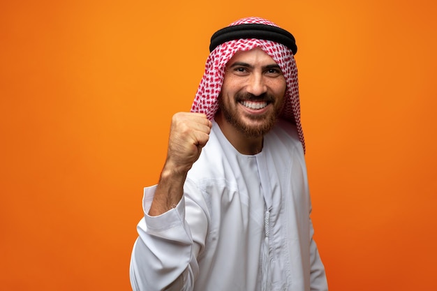 Succès souriant jeune homme arabe célébrant la victoire sur fond orange