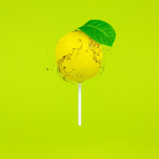 Sucette au citron avec bâton et éclaboussures sur fond vert clair. Concept d'été minimal de nourriture de bonbons.