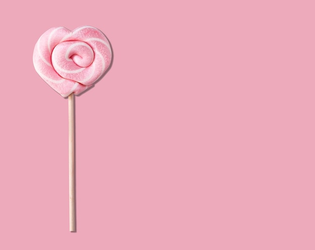 Photo sucette rose en forme de coeur sur un bâton sur fond rose pastel