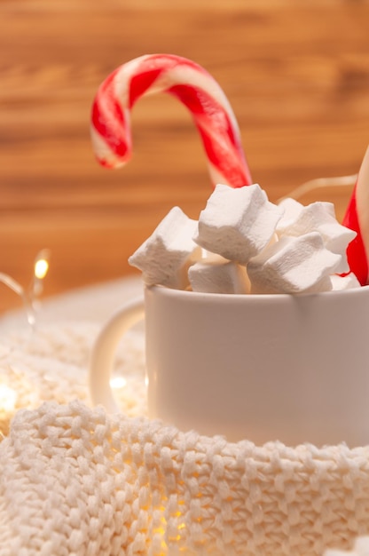 Sucettes et guimauves dans une tasse blanche avec un plaid sur un fond en bois Bonbons de Noël