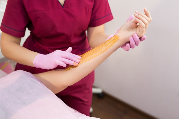 Sucre. Concept de beauté. Jeune belle fille aux cheveux noirs obtient la procédure pour le sucre liquide d'épilation. Concept d'épilation et de beauté - procédure d'épilation à portée de main sur une belle femme