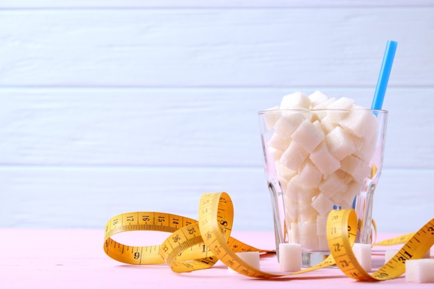 Sucre dans un verre et ruban à mesurer sur fond coloré