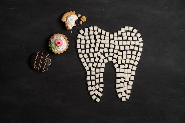 Le sucre détruit l'émail des dents conduit à la carie dentaire Les cubes de sucre blanc forment une dent carrée de sucre brun fond noir Santé et médecine Concept de stomatologie Les aliments sucrés détruisent les dents