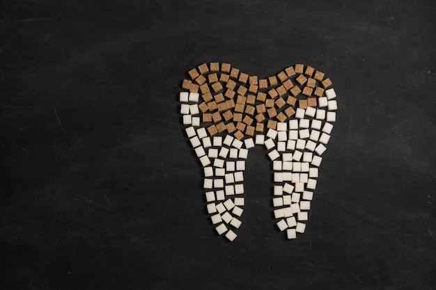Le sucre détruit l'émail des dents conduit à la carie dentaire Les cubes de sucre blanc forment une dent carrée de sucre brun fond noir Santé et médecine Concept de stomatologie Les aliments sucrés détruisent les dents