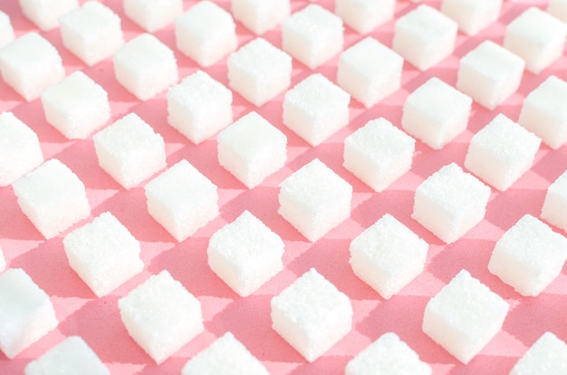 Sucre raffiné sur fond rose. Cubes de sucre doux et blanc en forme géométrique. Ombres dures et stores.