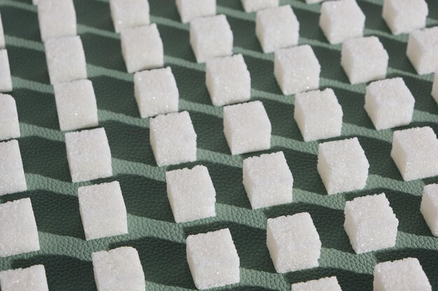 Sucre raffiné sur fond vert. Cubes de sucre doux et blanc en forme géométrique. Ombres dures.