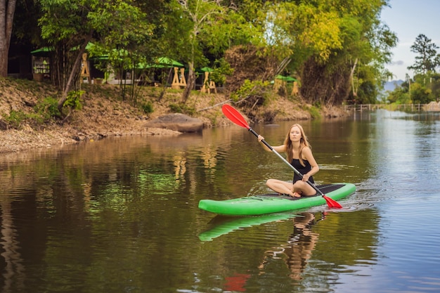 SUP Stand up paddle board femme paddle board sur le lac debout heureux sur paddleboard sur l'eau bleue Photo d'action de jeune femme sur Paddle Board