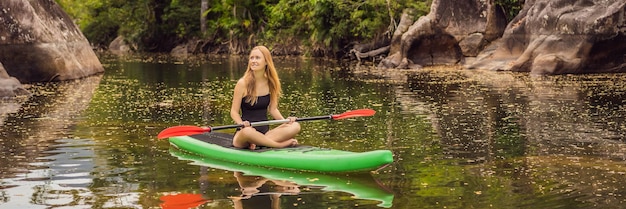 Photo sup stand up paddle board femme à la pagaie sur le lac se tenant heureuse sur la pagaie dans l'eau bleue clip d'action d'une jeune femme sur la pataie banner long format