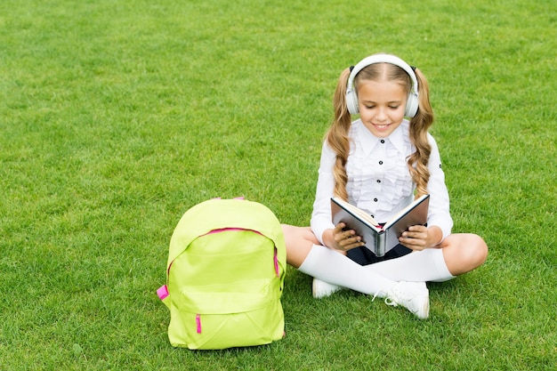 Super endroit pour apprendre. petite fille tenir un livre. littérature pour enfants. développement de l'enfance. travailler avec un cahier. retour à l'école. enfant étudie dans le parc. détendez-vous sur l'herbe verte avec un livre. écouter de la musique en ligne.