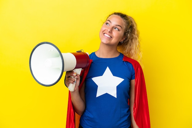 Super héros femme isolée sur fond jaune tenant un mégaphone et levant les yeux en souriant