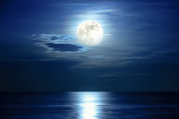 Super pleine lune et nuages dans le ciel bleu au-dessus de l'horizon océanique à minuit, le clair de lune reflète la surface de l'eau et les vagues, Belle vue sur le paysage naturel sur la scène nocturne de la mer pour le fond