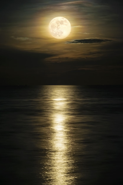 Super pleine lune et nuages dans le ciel jaune au-dessus de l'horizon océanique à minuit, le clair de lune reflète la surface de l'eau et la vague, Belle vue sur le paysage naturel sur la scène nocturne de la mer pour le fond