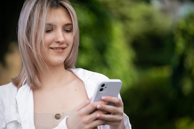 Superbe belle jeune femme aux cheveux blonds messagerie sur le smartphone à l'arrière-plan de la rue de la ville jolie fille ayant une conversation téléphonique intelligente sur la rue de la ville