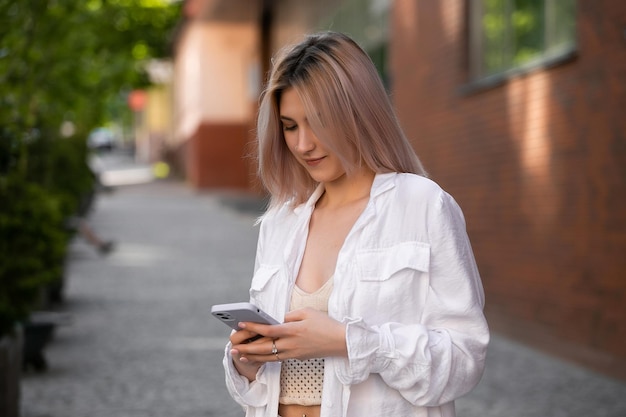 Superbe belle jeune femme aux cheveux blonds messagerie sur le smartphone à l'arrière-plan de la rue de la ville jolie fille ayant une conversation téléphonique intelligente sur la rue de la ville