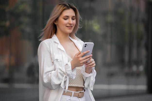 Superbe belle jeune femme aux cheveux blonds messagerie sur le smartphone à l'arrière-plan de la rue de la ville jolie fille ayant une conversation téléphonique intelligente sur la rue de la ville