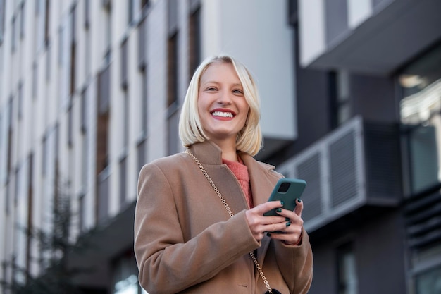 Superbe belle jeune femme aux cheveux blonds messagerie sur le smartphone à l'arrière-plan de la rue de la ville. jolie fille ayant une conversation téléphonique intelligente