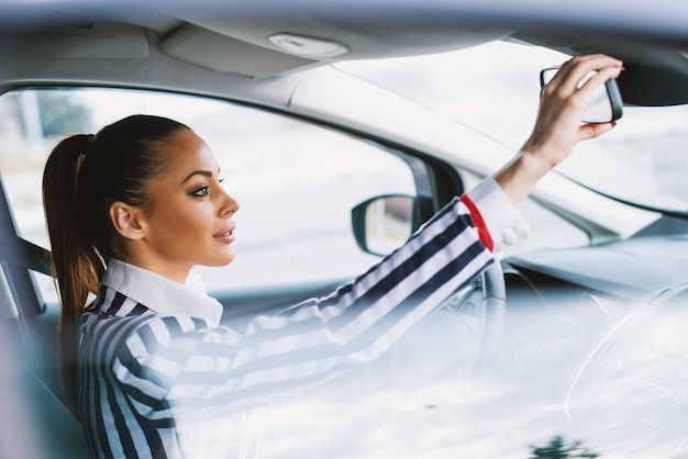 Superbe brune fixant le rétroviseur de voiture.