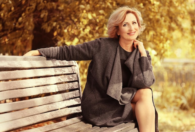 Superbe femme d'âge moyen assis sur un banc à l'automne parc