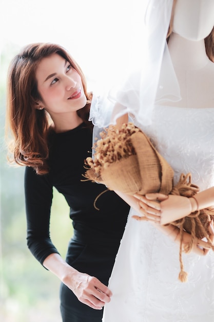 Une superbe femme asiatique se prépare à être la mariée et à revoir la robe de mariée en marionnette mannequin avec le sourire et le bonheur.