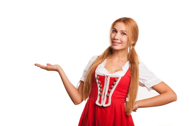 Photo superbe femme bavaroise aux cheveux rouges sexy souriant gaiement à la caméra tenant l'espace copie sur sa main. belle serveuse d'oktoberfest en costume allemand traditionnel