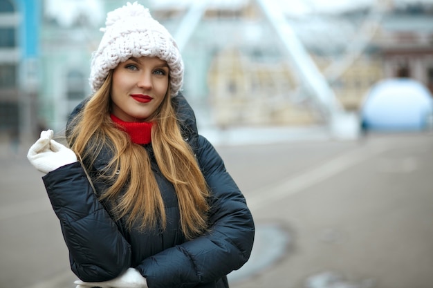 Superbe femme blonde avec du rouge à lèvres portant une casquette tricotée, profitant d'une promenade en ville. Espace pour le texte