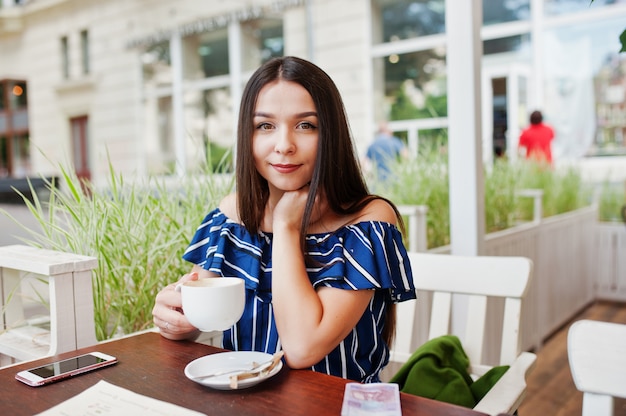 Superbe femme brune assise sur la table à café avec une tasse de café.