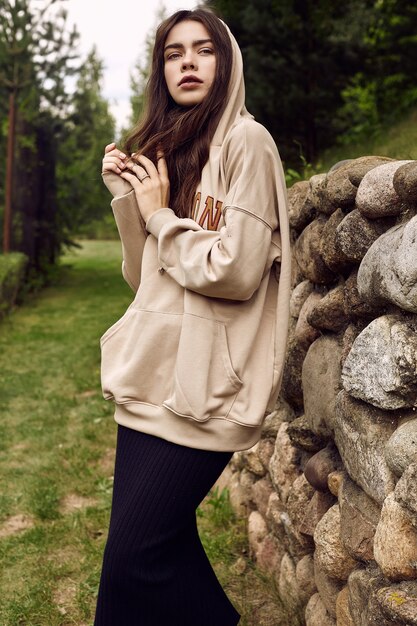 Superbe femme brune à la mode à capuche dans l'allée du jardin