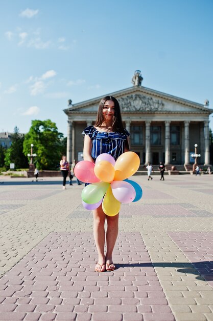 Superbe femme brune à la rue de la ville avec des ballons à la main.