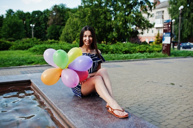 Superbe femme brune à la rue de la ville avec des ballons à la main.