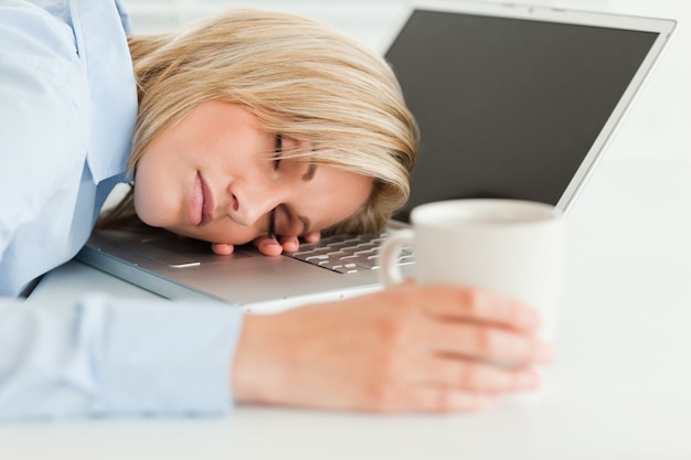 Superbe femme dormant sur son ordinateur portable avec une tasse de café à la main