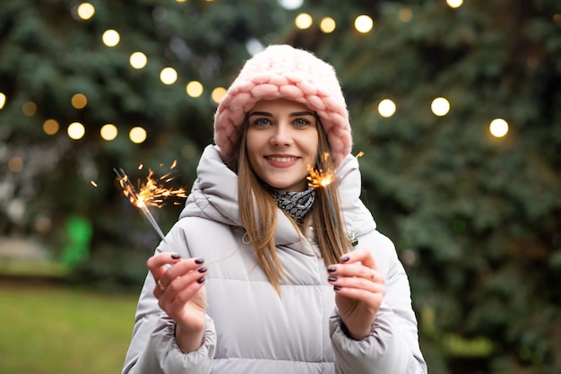 Superbe femme souriante s'amusant avec des cierges magiques près de l'arbre du nouvel an