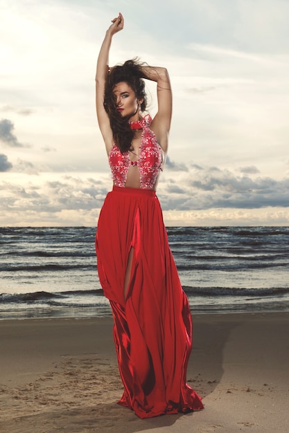 Superbe femme vêtue d'une belle robe rouge sur la plage pendant le coucher du soleil