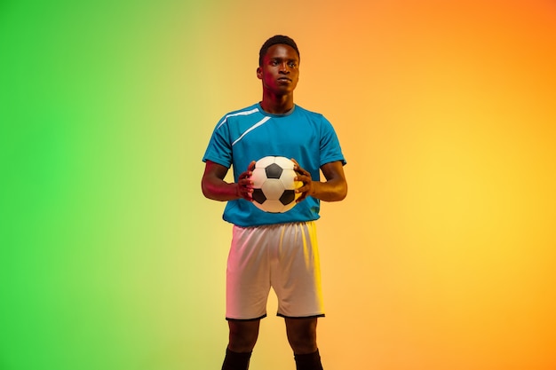 Photo superbe. football masculin afro-américain, entraînement de joueur de football en action isolé sur fond de studio dégradé à la lumière du néon. concept de mouvement, action, réalisations, mode de vie sain. culture jeunesse