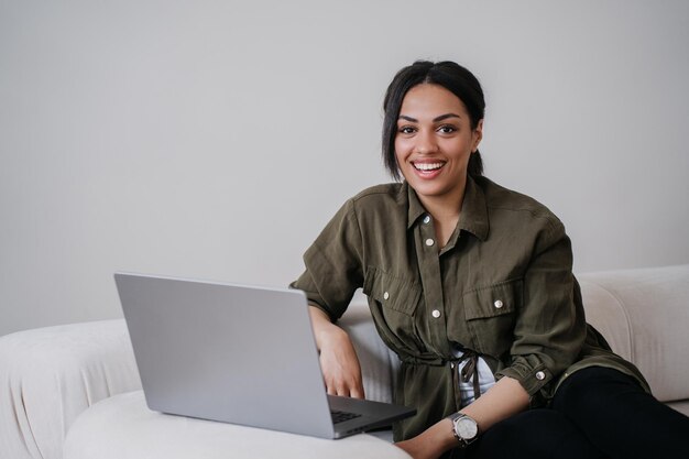 Superbe jeune femme afro-américaine déterminée dans un sourire décontracté à pleines dents sur un canapé confortable a l'air heureux