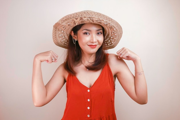 Superbe jeune femme asiatique forte avec une robe orange et un chapeau de paille montrant des biceps et un concept fort de fille indonésienne souriante