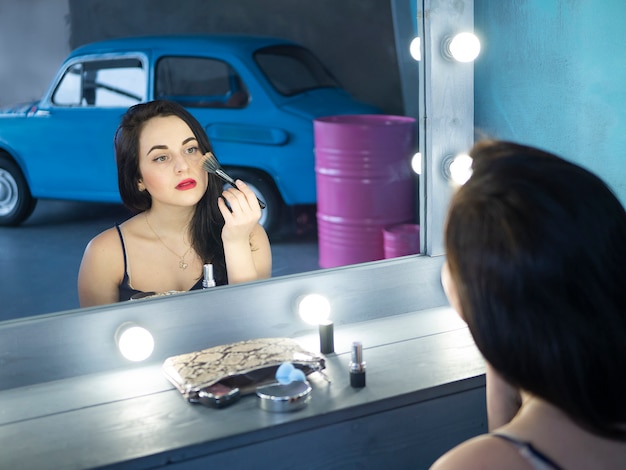 Superbe jeune femme aux cheveux bruns souriante, posant, à l&#39;aide d&#39;un pinceau à maquillage pour appliquer le blush.