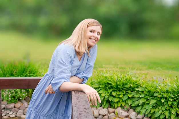 Superbe jeune femme blonde en robe bleue élégante heureuse dans les conversations de jardin