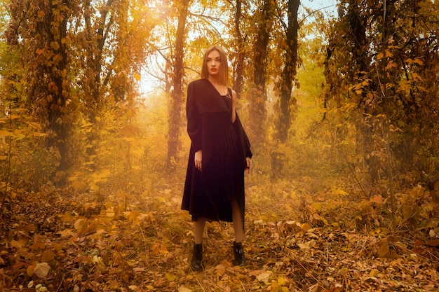 Superbe jeune fille blonde en manteau noir à la recherche de suite dans la forêt d'automne dorée