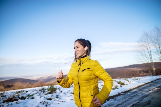 Superbe jeune fille en veste jaune s'amuser tout en courant dans la nature recouverte de neige.