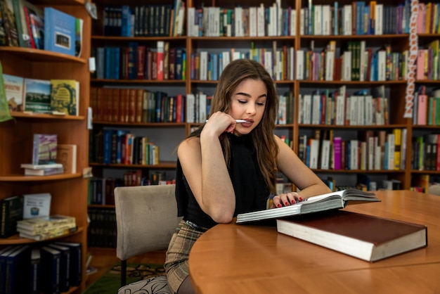 Superbe jeune professeure vêtue de vêtements noirs stricts, étudiant des livres dans la bibliothèque. Notion de bibliothèque