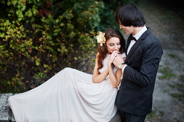 Superbe mariée aux longs cheveux bouclés et le marié assis près de l'autre à fond de feuilles vertes, photo de mariage, beau couple, jour de mariage.